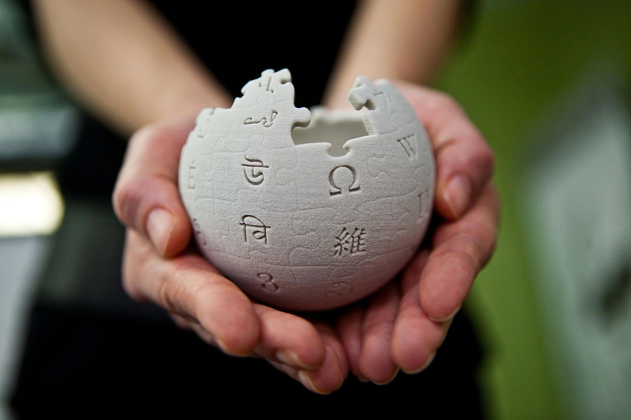 Hände halten Wikipedia-Puzzleball
