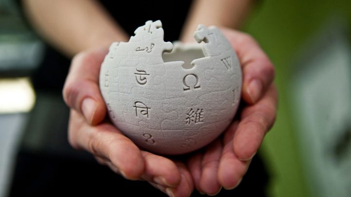 Hände halten Wikipedia-Puzzleball