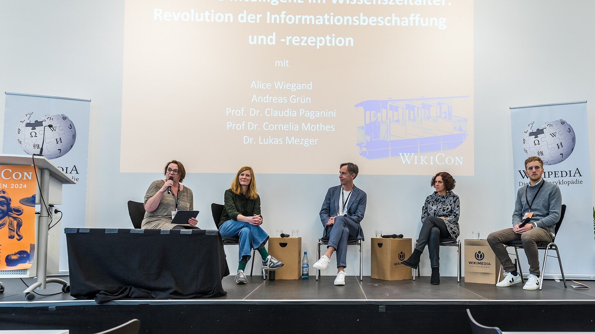 Alice Wiegand, Prof. Dr. Cornelia Mothes, Prof. Dr. Claudia Paganini, Dr. Lukas Mezger (Gnom) und Andreas Grün (ZDF) sitzen auf einer Bühne und sprechen über "Künstliche Intelligenz im Wissenszeitalter".