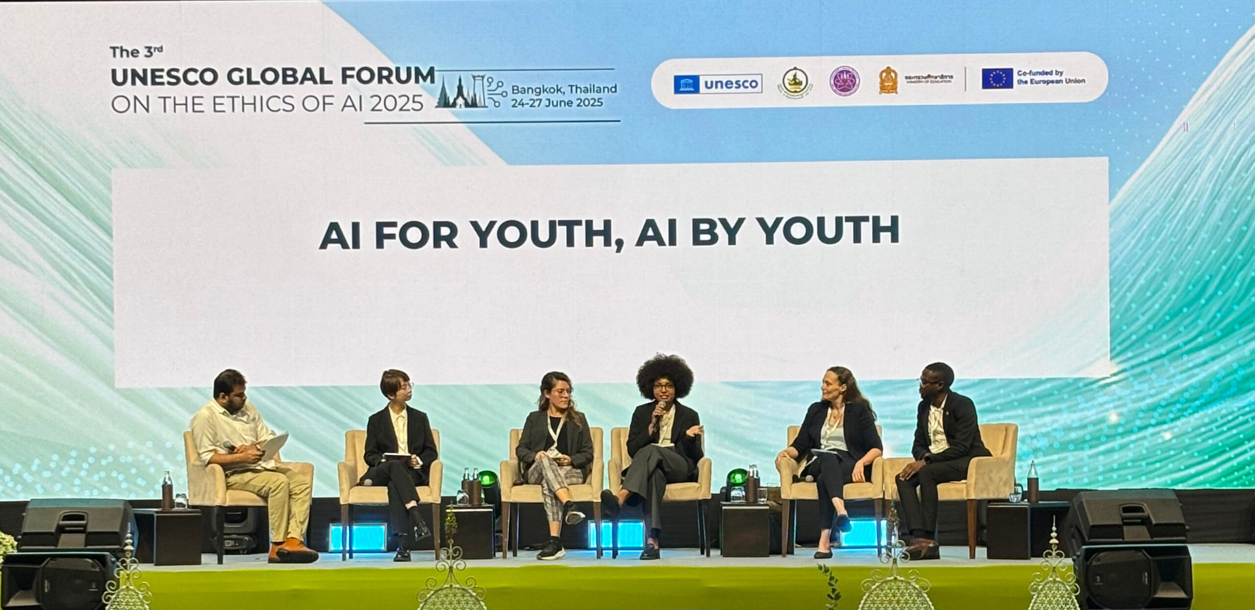 Sophia Longwe diskutiert mit Teilnehmenden beim AI for Youth Forum im Rahmen des UNESCO Global Forum on the Ethics of AI. Zu sehen sind Longwe und fünf weitere Menschen, die auf einer Bühne sitzen und miteinander sprechen. Das Global Forum on the Ethics of AI fand 2025 in Bangkok statt.