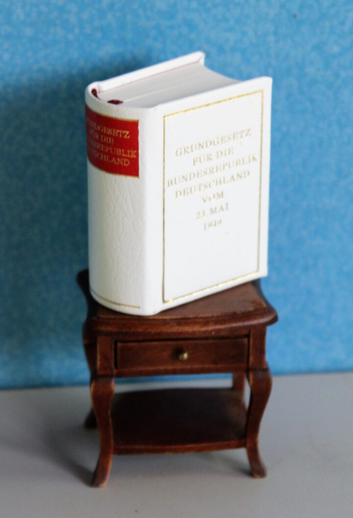Eine Miniaturausgabe des Grundgesetzes für die Bundesrepublik Deutschland steht auf einem Miniaturtisch.