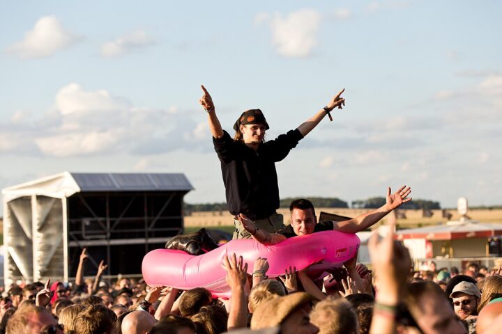 Zwei Männer im rosa Schlauchboot crowdsurfen über eine Menschenmenge.