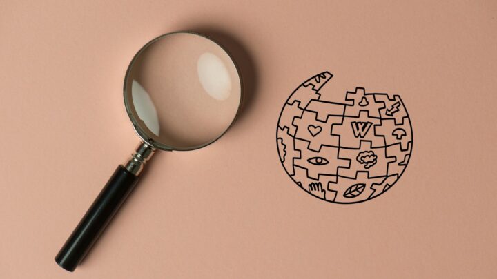 Eine Lupe liegt links neben einer Illustration des Wikipedia-Puzzleballs.