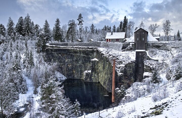 Ein Blick in eine Winterlandschaft: Altmodische Industriegebäude, halb von Bäumen umgeben, sind von dünnem Schnee bedeckt.
