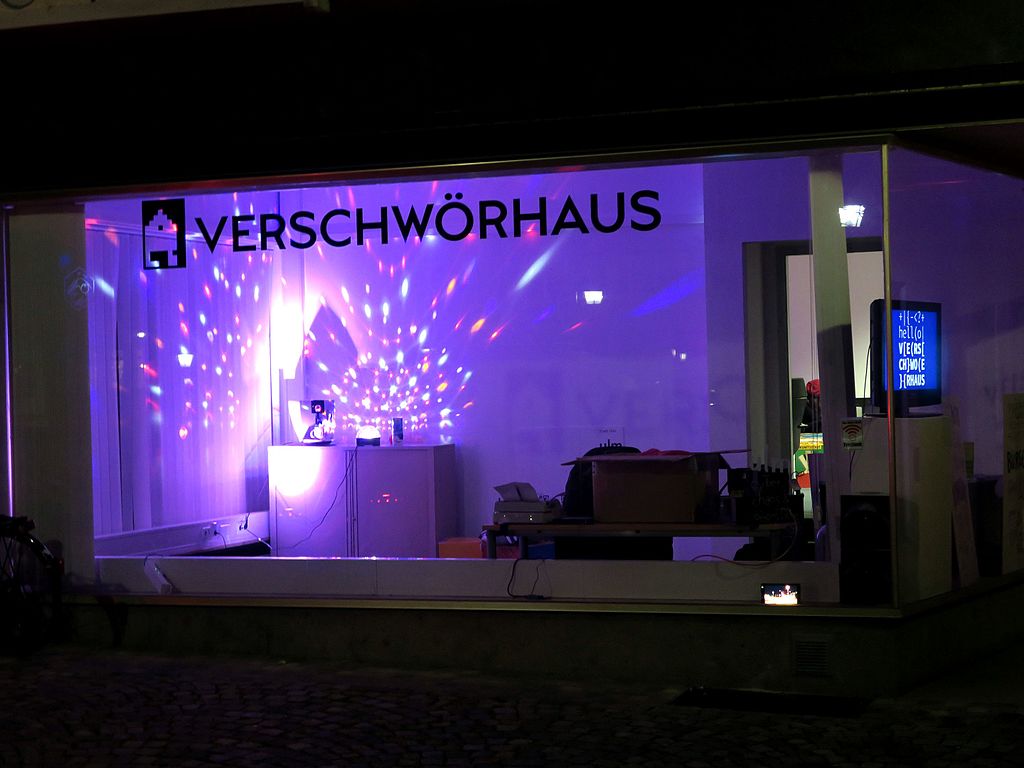 Ein Schaufenster mit der Aufschrift Verschwörhaus zeigt eine lilafarbene Lichtershow.