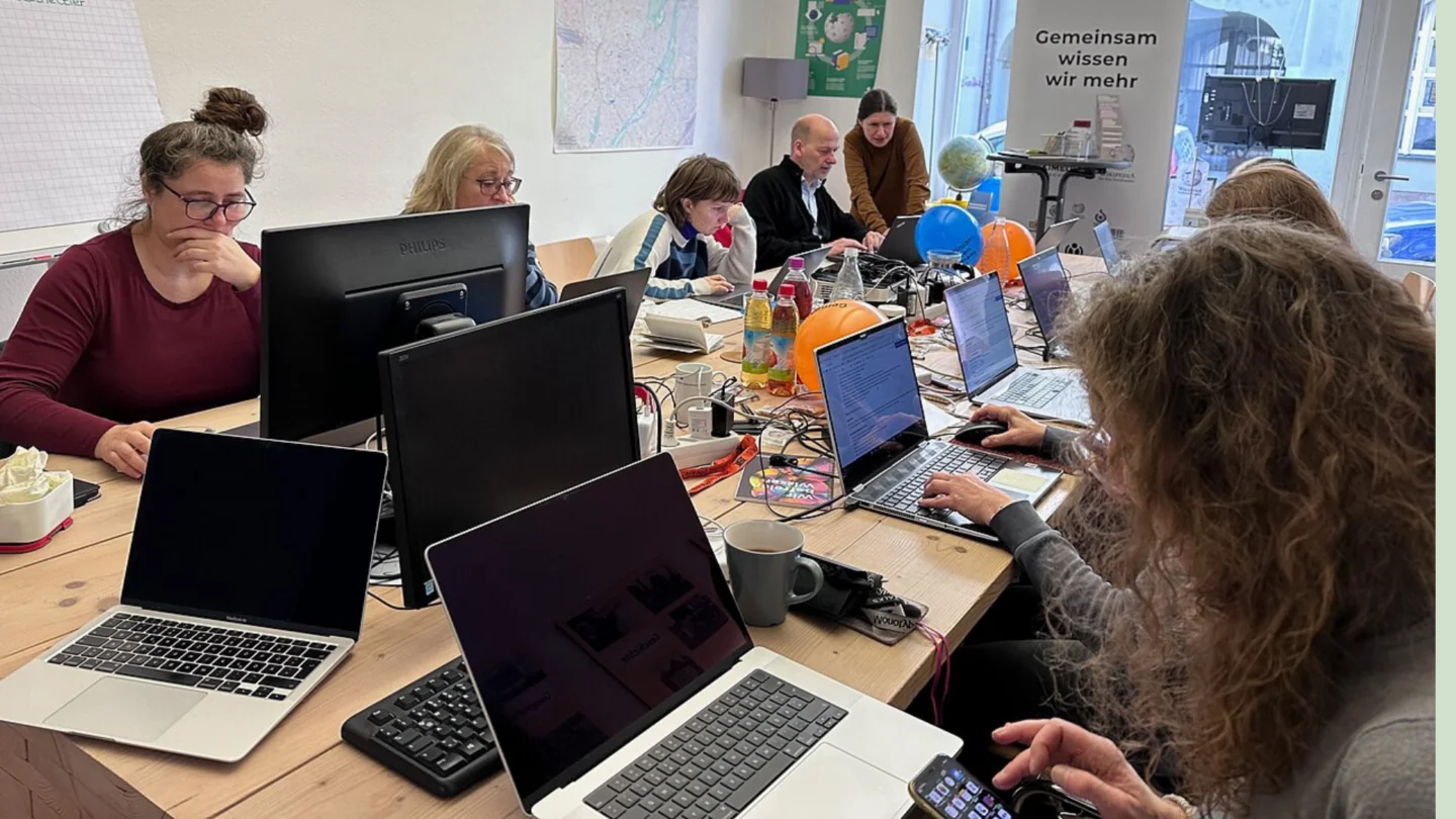 Menschen sitzen mit Laptops an einem Tisch und arbeiten.