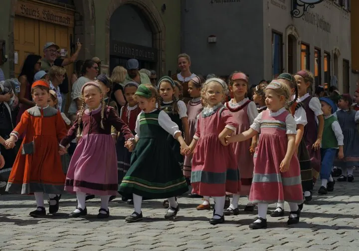 Kinder in Trachten laufen Hand in Hand eine Straße hinunter.