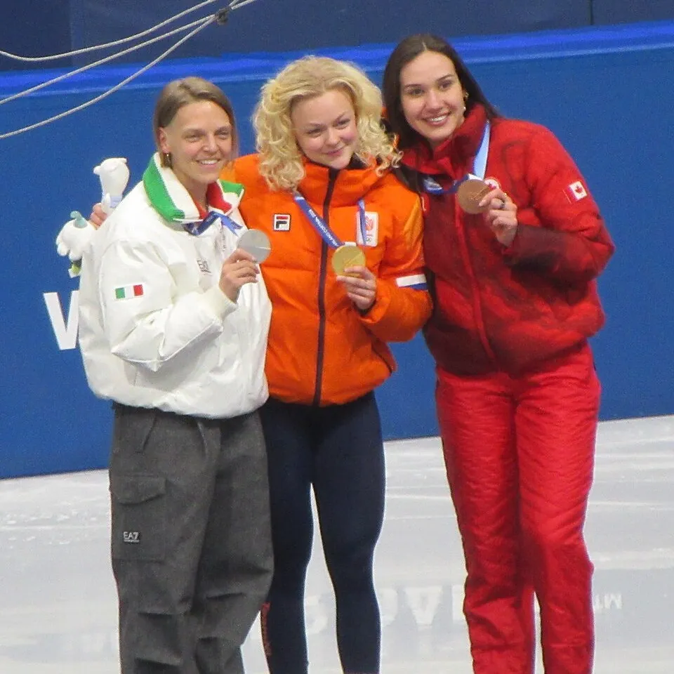 Drei Sportlerinnen in Winterkleidung zeigen ihre olympischen Medaillen in die Kamera