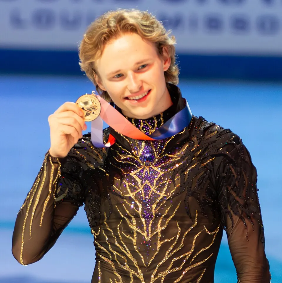 Ilia Malinin hält lächelnd seine Goldmedaille hoch