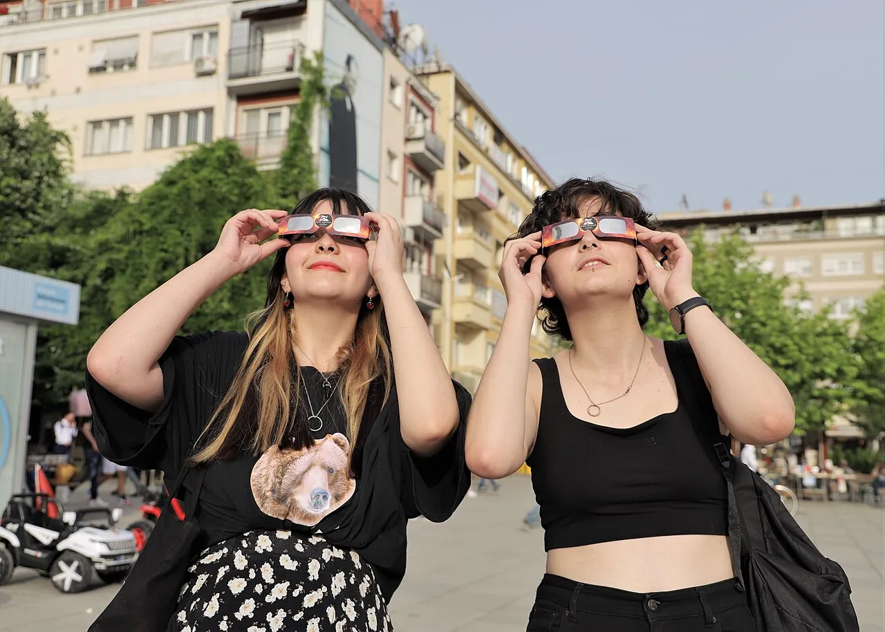 Zwei Menschen schauen mit einer Sonnenfinsternisbrille in den Himmel.