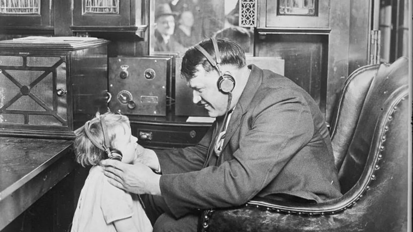 Ein Mann und sein Kind hören im Zug Radio über Kopfhörer. Schwarzweiß-Bild von 1925.