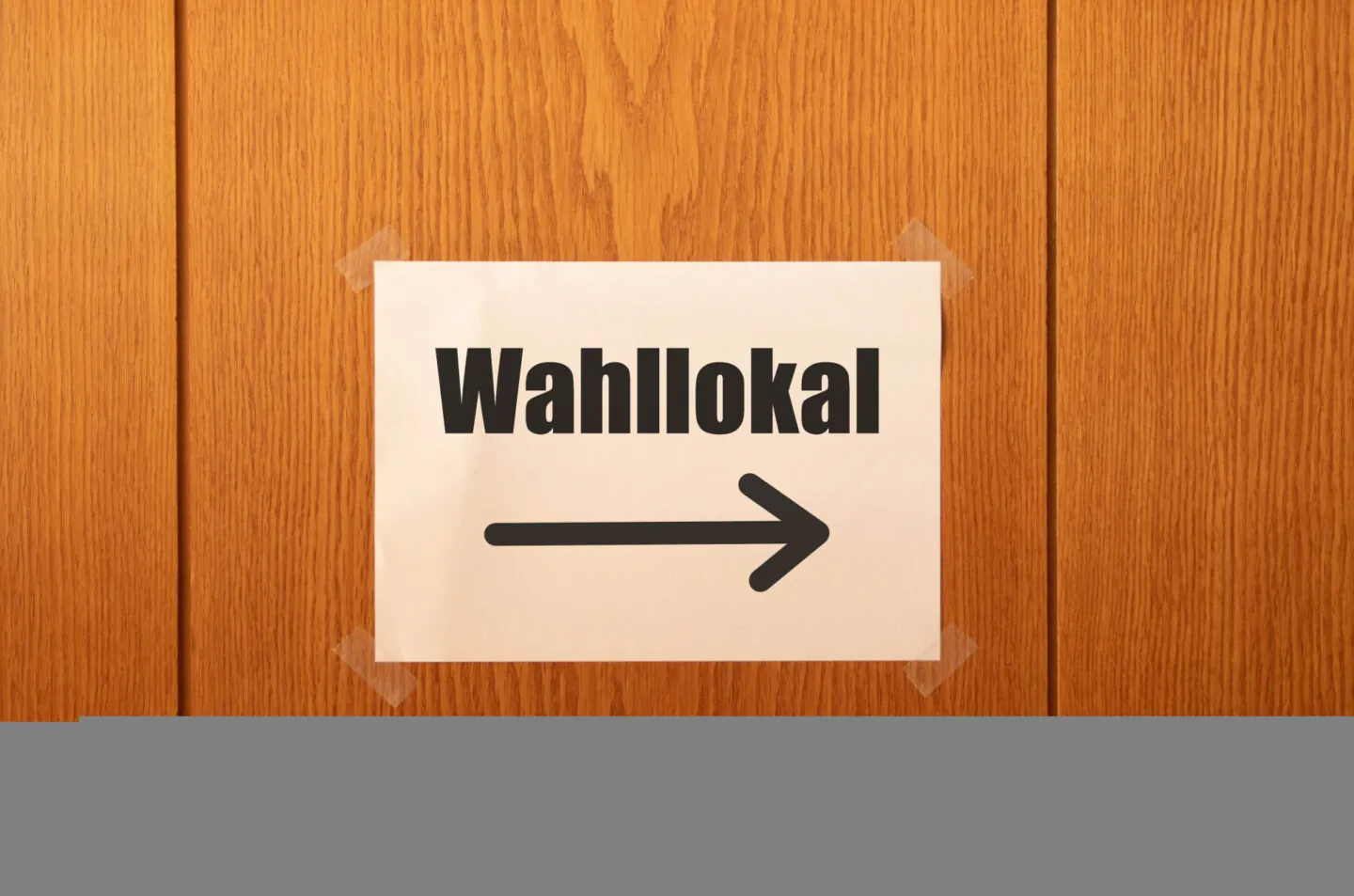 Das Foto zeigt ein weißes Schild aud dem in schwarzen Buchstaben steht: Wahllokal. darunter ist ein Pfeil zu sehen, der nach rechts weist. Das Schild ist an eine Wand oder Tür aus Holpanelen angebracht. Foto: Marco Verch, CC BY 2.0